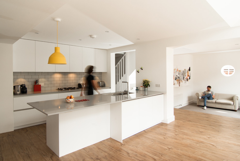 Inspiration for a contemporary galley kitchen in London with flat-panel cabinets, white cabinets, grey splashback, subway tile splashback, light hardwood floors and a peninsula.