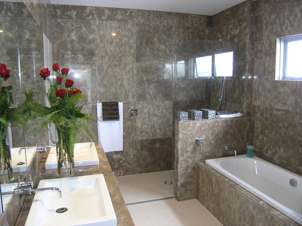 This is an example of a large modern master bathroom in Brisbane with a drop-in sink, flat-panel cabinets, white cabinets, marble benchtops, a drop-in tub, an open shower, a wall-mount toilet, brown tile, stone slab, brown walls and ceramic floors.