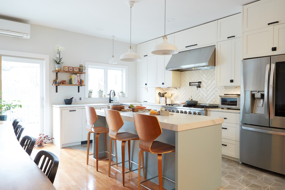 Mid-sized transitional l-shaped eat-in kitchen in New York with white cabinets, quartzite benchtops, white splashback, ceramic splashback, stainless steel appliances, with island, shaker cabinets, grey floor and grey benchtop.
