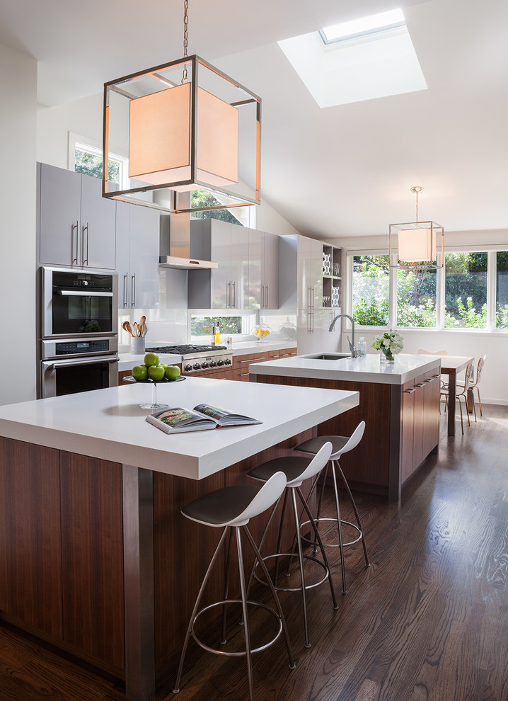 Design ideas for a contemporary eat-in kitchen in San Francisco with an undermount sink, flat-panel cabinets, grey cabinets, quartz benchtops, white splashback, glass sheet splashback, stainless steel appliances, dark hardwood floors and multiple islands.