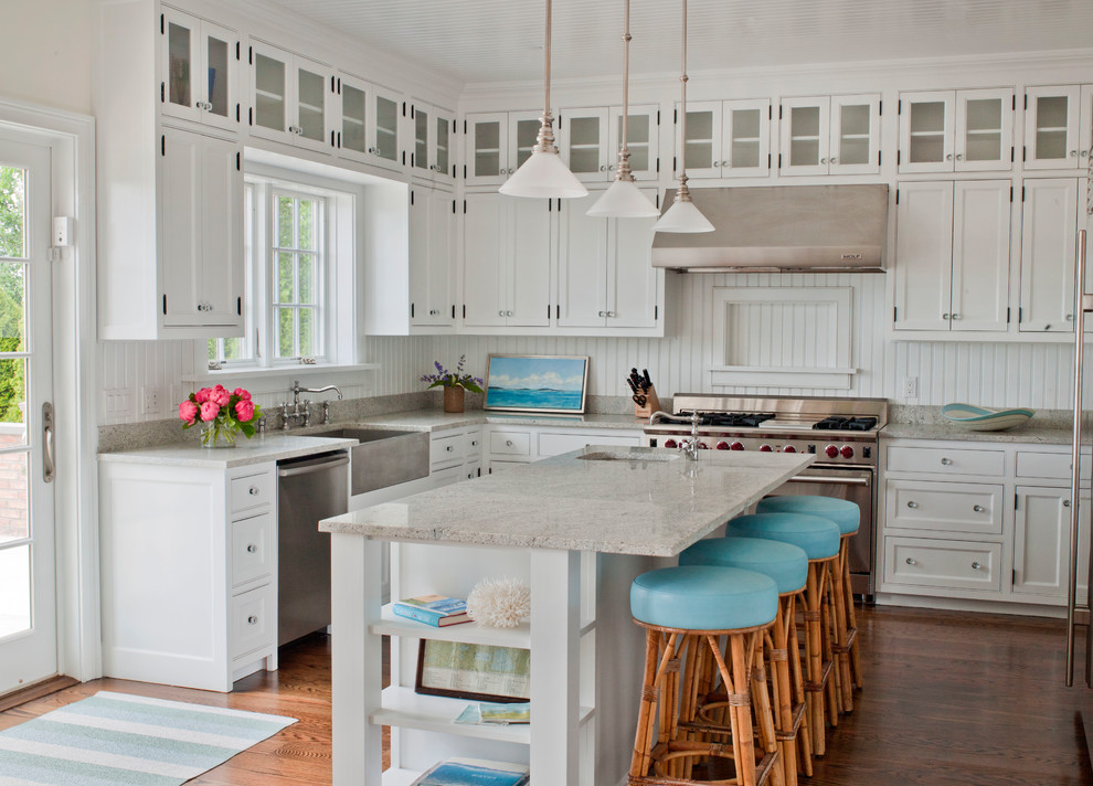 Beach style kitchen in New York with a farmhouse sink, beaded inset cabinets, white cabinets, white splashback, timber splashback, stainless steel appliances, medium hardwood floors, with island and grey benchtop.