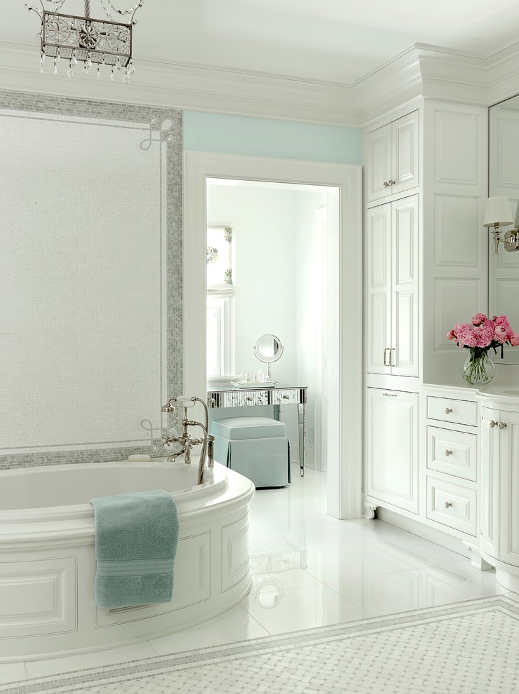 This is an example of a beach style bathroom in St Louis with raised-panel cabinets, white cabinets, a drop-in tub, white tile and white floor.
