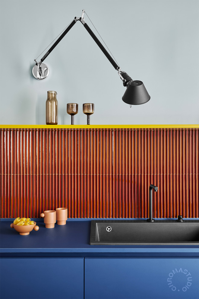 Photo of a mid-sized contemporary galley open plan kitchen in Milan with a single-bowl sink, blue cabinets, orange splashback, mosaic tile splashback, black appliances, concrete floors, with island, blue floor and blue benchtop.