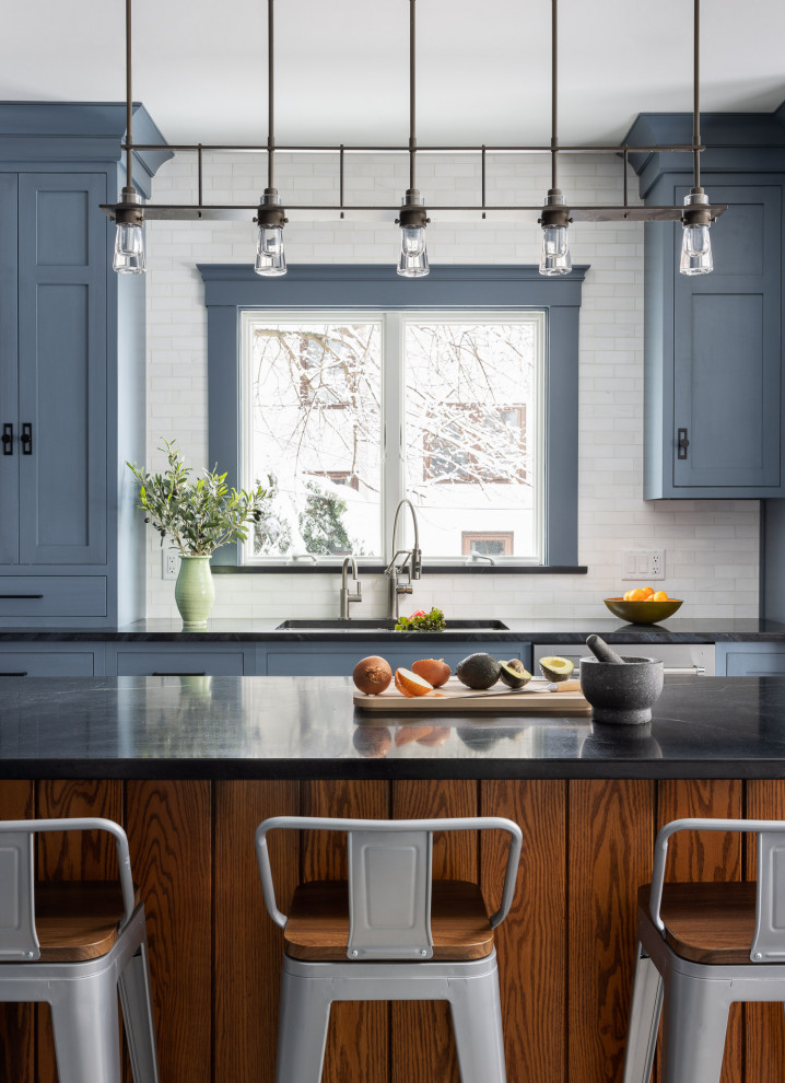 Mid-sized eclectic l-shaped kitchen with an undermount sink, recessed-panel cabinets, blue cabinets, soapstone benchtops, white splashback, stainless steel appliances, porcelain floors, with island, grey floor and black benchtop.