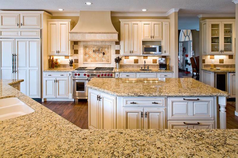 Inspiration for a large traditional open plan kitchen in Phoenix with a double-bowl sink, raised-panel cabinets, white cabinets, granite benchtops, brown splashback, ceramic splashback, stainless steel appliances, medium hardwood floors, multiple islands and brown floor.