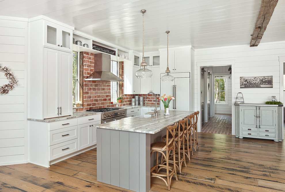 This is an example of a country l-shaped kitchen in Charleston with a farmhouse sink, shaker cabinets, white cabinets, red splashback, brick splashback, stainless steel appliances, medium hardwood floors, with island and brown floor.