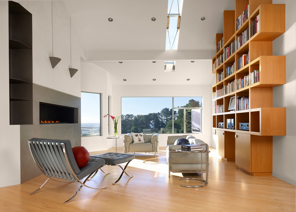 This is an example of a contemporary open concept family room in San Francisco with a library, white walls, light hardwood floors and a ribbon fireplace.