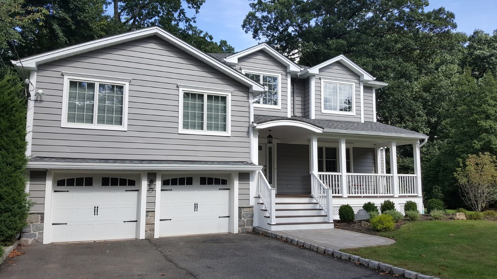 This is an example of a large traditional split-level grey house exterior in New York with vinyl siding, a gable roof and a shingle roof.