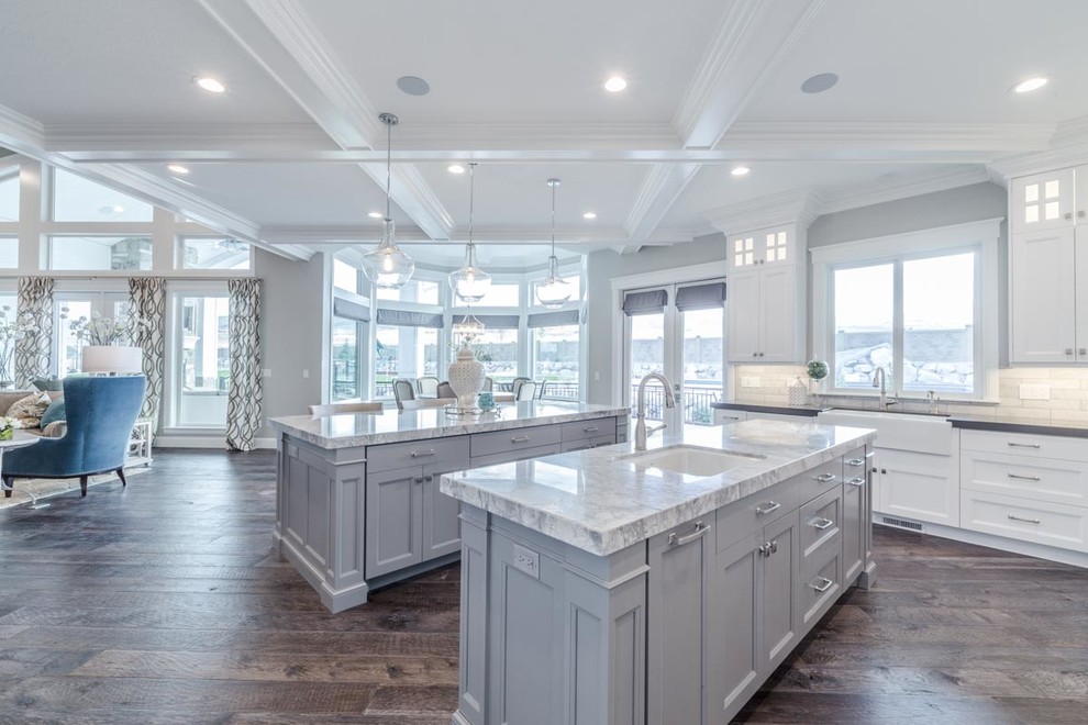 Design ideas for a large transitional u-shaped open plan kitchen in Salt Lake City with an undermount sink, recessed-panel cabinets, white cabinets, marble benchtops, white splashback, subway tile splashback, stainless steel appliances, medium hardwood floors, multiple islands and brown floor.