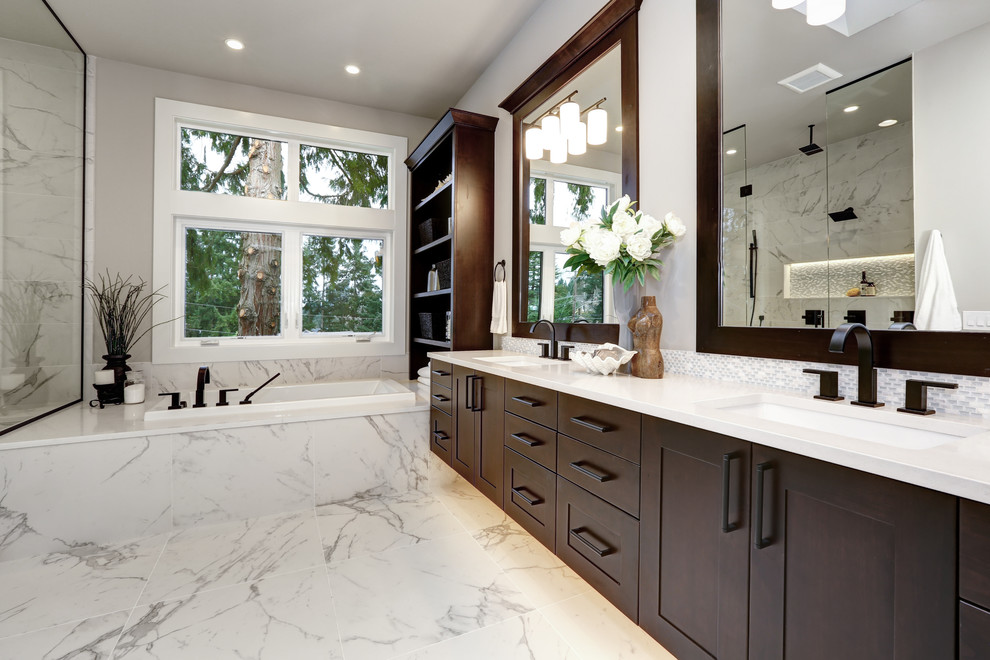 This is an example of a large modern master bathroom in DC Metro with shaker cabinets, brown cabinets, a drop-in tub, a curbless shower, a two-piece toilet, white tile, porcelain tile, white walls, porcelain floors, an undermount sink, engineered quartz benchtops, white floor, a hinged shower door and white benchtops.