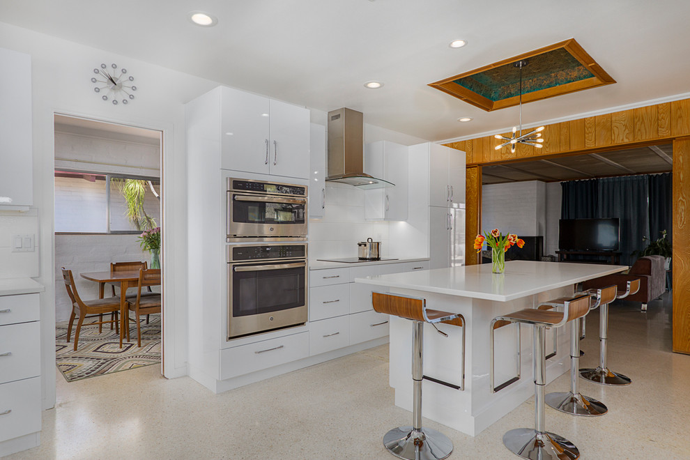 This is an example of a mid-sized midcentury galley separate kitchen in Phoenix with an undermount sink, flat-panel cabinets, white cabinets, quartz benchtops, green splashback, glass tile splashback, stainless steel appliances, terrazzo floors, with island, beige floor and white benchtop.