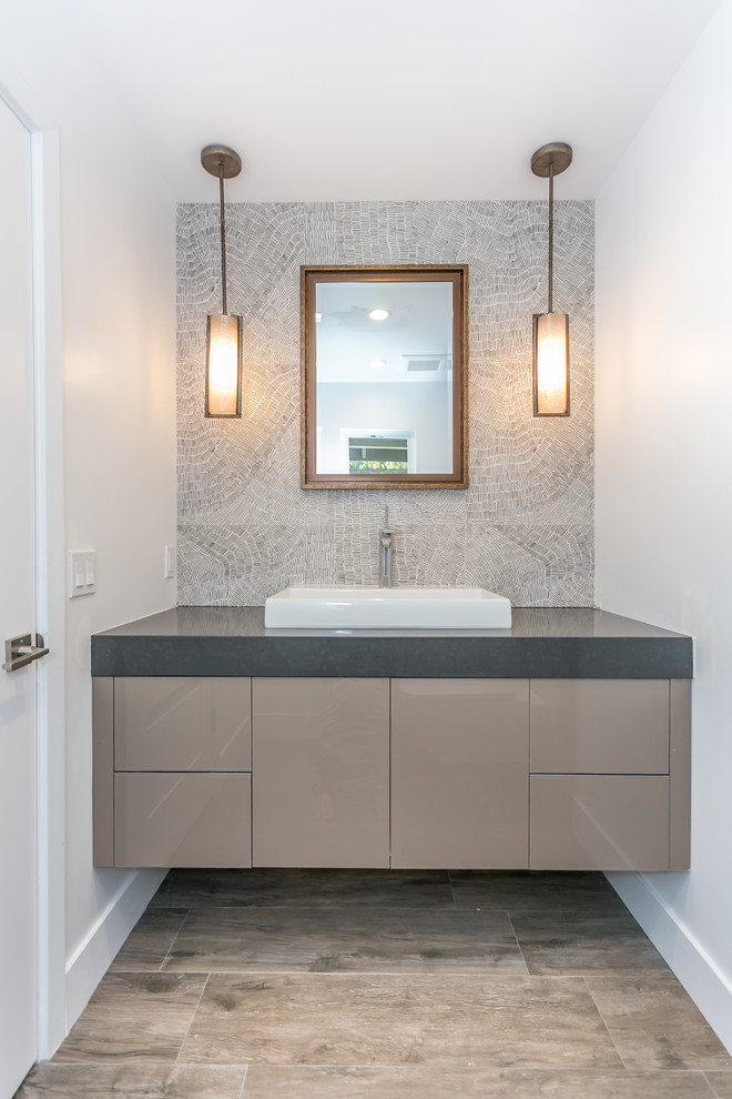 Photo of a mid-sized modern bathroom in Los Angeles with a drop-in sink, brown cabinets, engineered quartz benchtops, a wall-mount toilet, white walls, ceramic floors and gray tile.