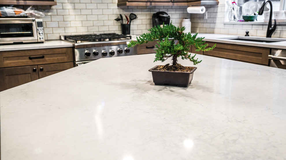 Example of a large transitional l-shaped vinyl floor and brown floor home design design in Seattle with an undermount sink, recessed-panel cabinets, medium tone wood cabinets, quartz countertops, white backsplash, subway tile backsplash, stainless steel appliances, an island and white countertops