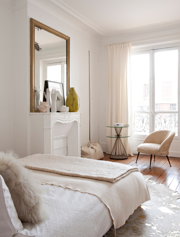Inspiration for a transitional bedroom in Paris with white walls, medium hardwood floors and a standard fireplace.