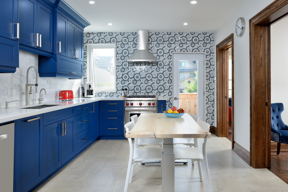 This is an example of a transitional l-shaped eat-in kitchen in Toronto with an undermount sink, shaker cabinets, blue cabinets, multi-coloured splashback, mosaic tile splashback, stainless steel appliances, no island, grey floor and white benchtop.