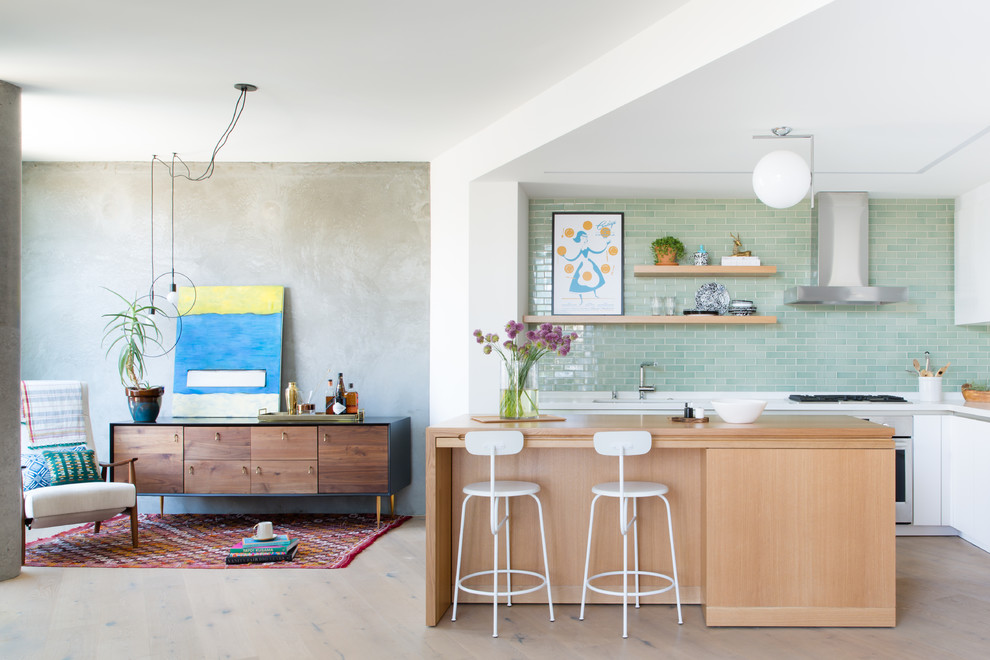 This is an example of a midcentury l-shaped open plan kitchen in San Francisco with flat-panel cabinets, white cabinets, green splashback, stainless steel appliances, light hardwood floors, with island, beige floor, white benchtop, an undermount sink and subway tile splashback.