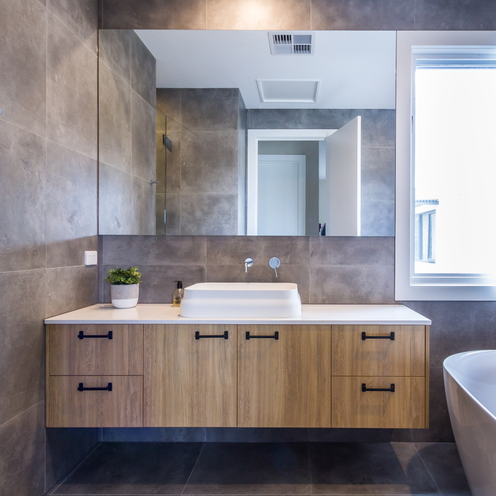 Design ideas for a mid-sized contemporary kids bathroom in Melbourne with flat-panel cabinets, medium wood cabinets, a freestanding tub, an alcove shower, gray tile, porcelain tile, grey walls, porcelain floors, a vessel sink, engineered quartz benchtops, grey floor, a hinged shower door and white benchtops.