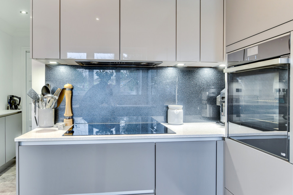 This is an example of a large modern grey and white u-shaped open plan kitchen in Sussex with a submerged sink, flat-panel cabinets, grey cabinets, quartz worktops, grey splashback, glass sheet splashback, integrated appliances, vinyl flooring, a breakfast bar, grey floors, white worktops and feature lighting.