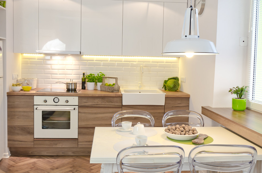 Contemporary eat-in kitchen in Other with a farmhouse sink, wood benchtops, flat-panel cabinets, medium wood cabinets, white splashback, subway tile splashback and white appliances.