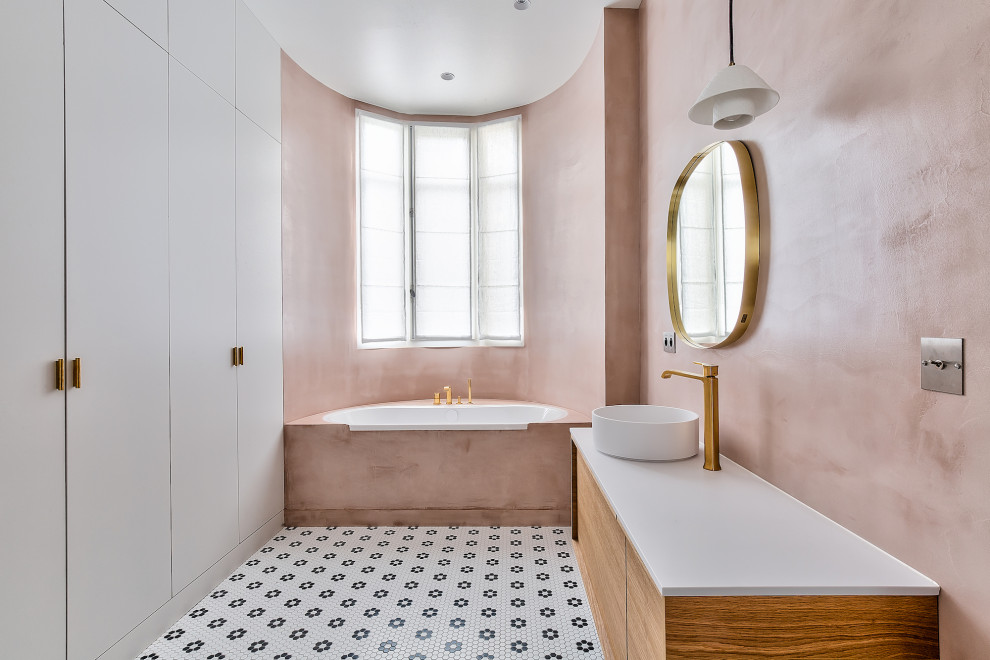 This is an example of a contemporary kids bathroom in Paris with flat-panel cabinets, medium wood cabinets, a drop-in tub, pink walls, mosaic tile floors, a vessel sink, multi-coloured floor, white benchtops, a single vanity and a floating vanity.