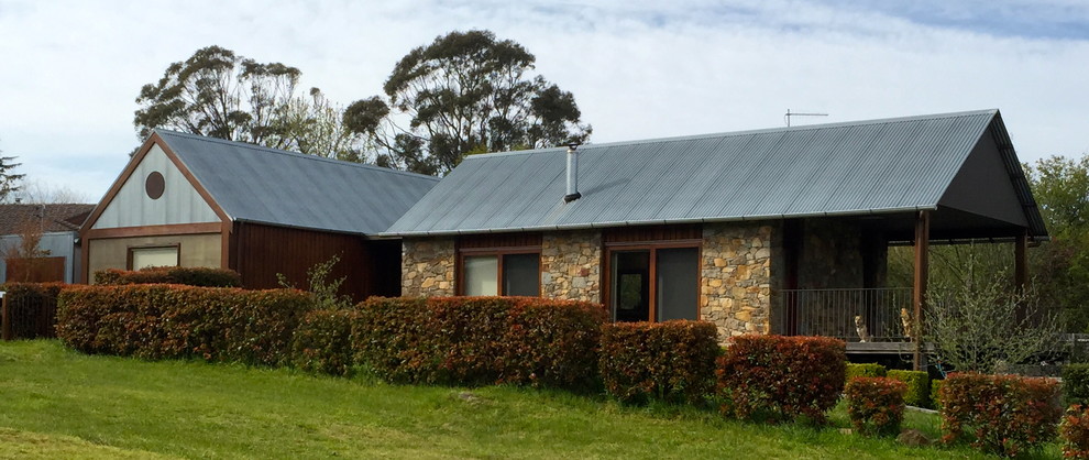 Photo of a large contemporary one-storey house exterior in Sydney with stone veneer, a gable roof and a metal roof.