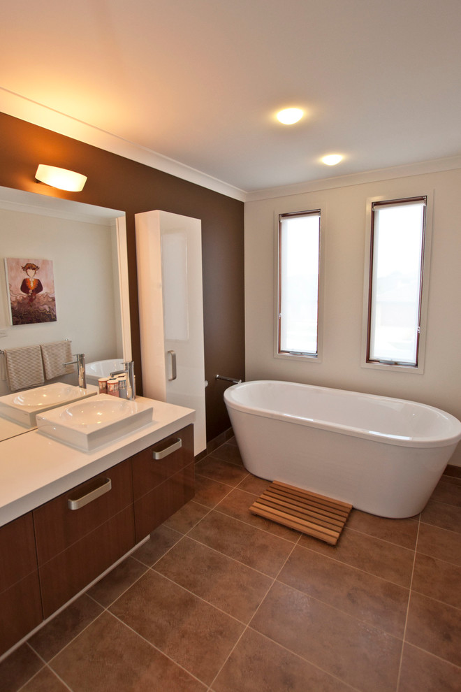 Photo of a large modern master bathroom in Melbourne with an integrated sink, furniture-like cabinets, medium wood cabinets, granite benchtops, a freestanding tub, brown tile, brown walls and light hardwood floors.