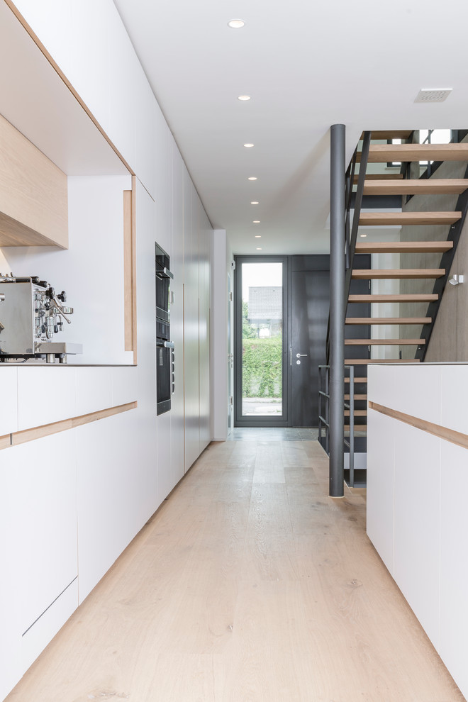 Küche mit integriertem Waschbecken, flächenbündigen Schrankfronten, weißen Schränken, Edelstahl-Arbeitsplatte, braunem Holzboden und Kücheninsel in Munich