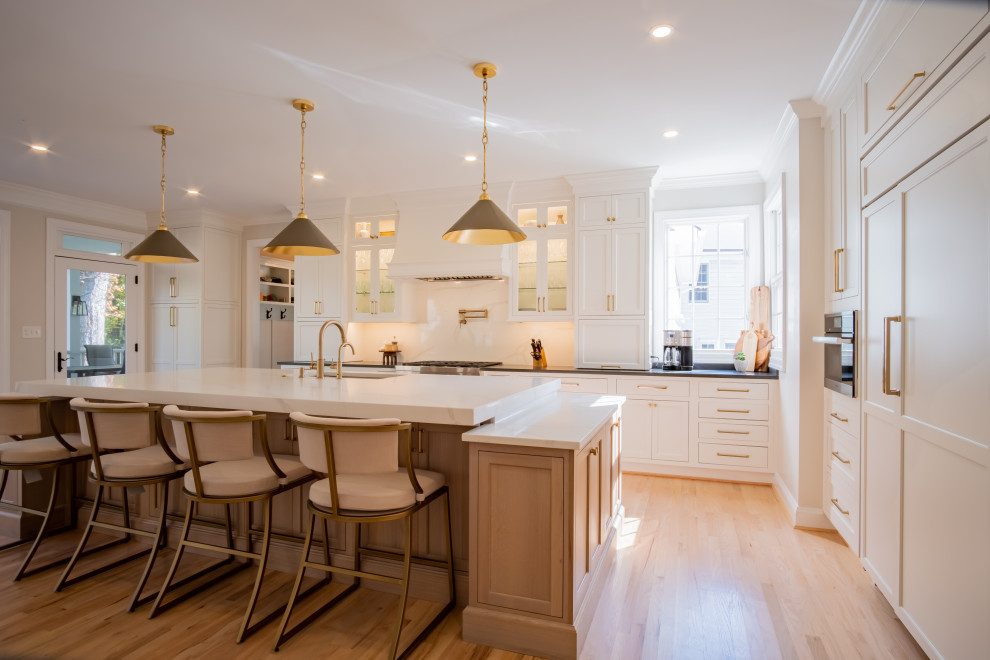 Photo of a large classic l-shaped kitchen/diner in DC Metro with a submerged sink, beaded cabinets, light wood cabinets, soapstone worktops, white splashback, engineered quartz splashback, stainless steel appliances, light hardwood flooring, an island, brown floors, black worktops and a wallpapered ceiling.