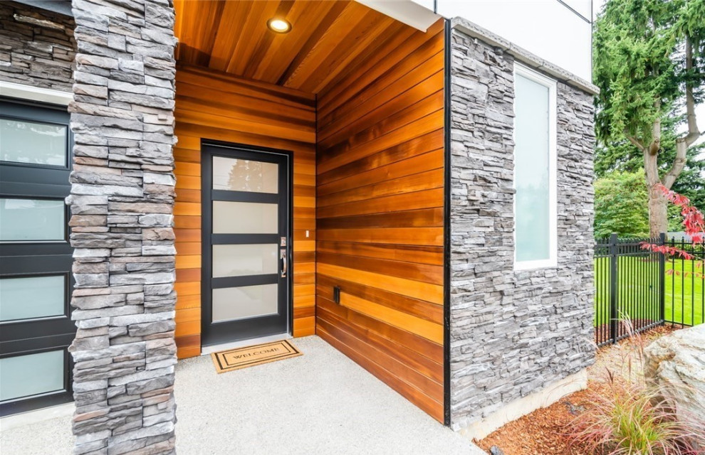 На фото: входная дверь среднего размера в современном стиле с коричневыми стенами, бетонным полом, одностворчатой входной дверью, черной входной дверью, серым полом, деревянным потолком и деревянными стенами
