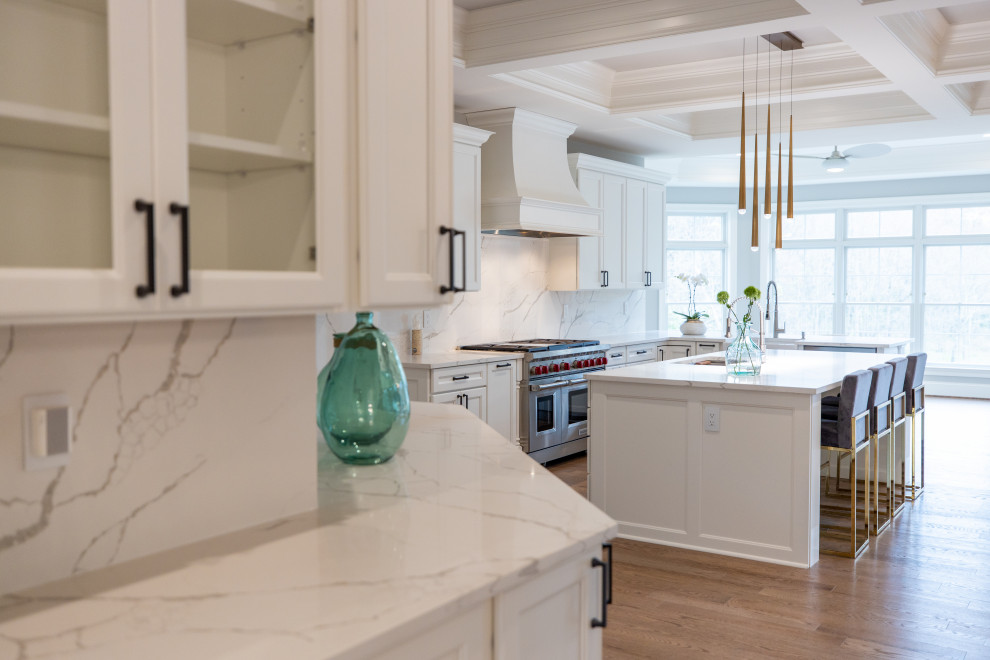Expansive classic u-shaped kitchen/diner in DC Metro with a submerged sink, shaker cabinets, white cabinets, engineered stone countertops, white splashback, engineered quartz splashback, stainless steel appliances, light hardwood flooring, an island, brown floors, white worktops and a drop ceiling.