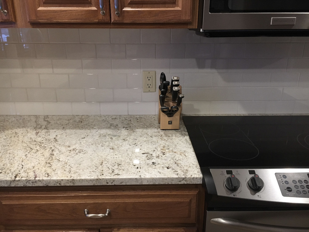 Example of a large transitional u-shaped medium tone wood floor eat-in kitchen design with an undermount sink, raised-panel cabinets, medium tone wood cabinets, granite countertops, white backsplash, ceramic backsplash, stainless steel appliances and an island
