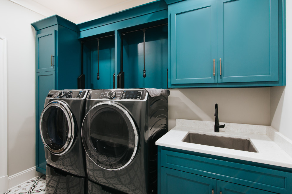 Esempio di una lavanderia multiuso costiera di medie dimensioni con lavello sottopiano, ante in stile shaker, ante blu, top in quarzo composito, pareti grigie, pavimento in cemento, lavatrice e asciugatrice affiancate, pavimento bianco e top bianco