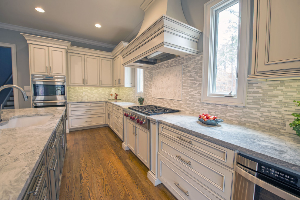 Large transitional l-shaped medium tone wood floor and brown floor eat-in kitchen photo with an undermount sink, gray backsplash, stainless steel appliances, two islands, beige cabinets, marble countertops and glass tile backsplash
