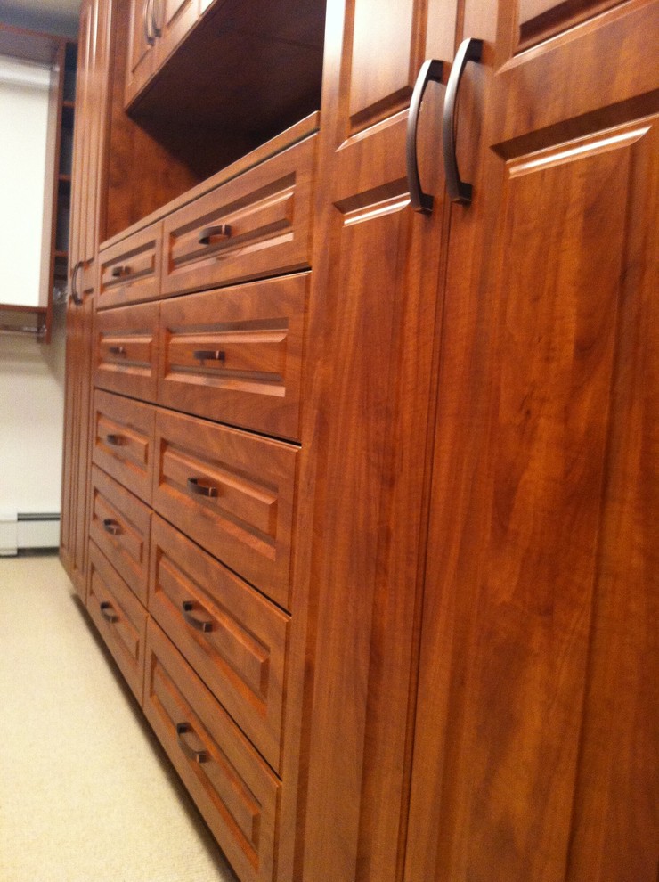 Mid-sized traditional gender-neutral walk-in wardrobe in Boston with raised-panel cabinets, medium wood cabinets and carpet.