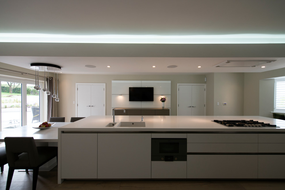 This is an example of an expansive contemporary eat-in kitchen in Wiltshire with an integrated sink, flat-panel cabinets, white cabinets, quartz benchtops, stainless steel appliances and with island.