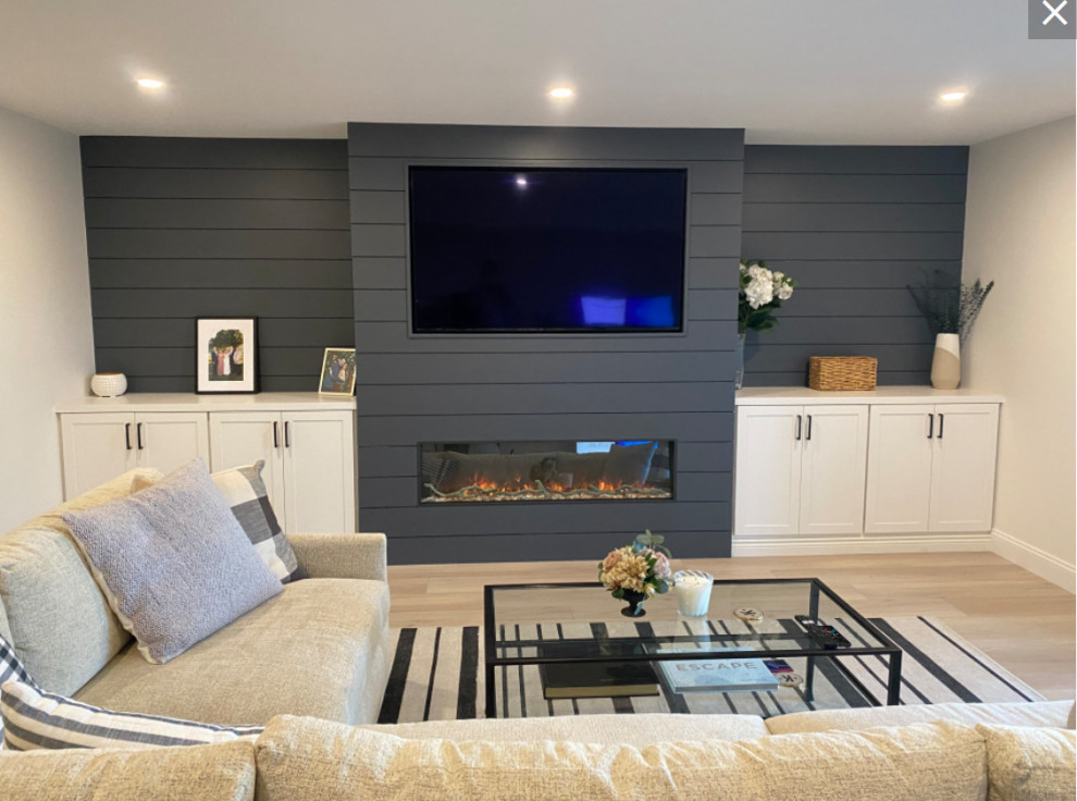 Example of a mid-sized country open concept light wood floor, beige floor and shiplap wall living room design in New York with beige walls, a standard fireplace, a shiplap fireplace and a wall-mounted tv