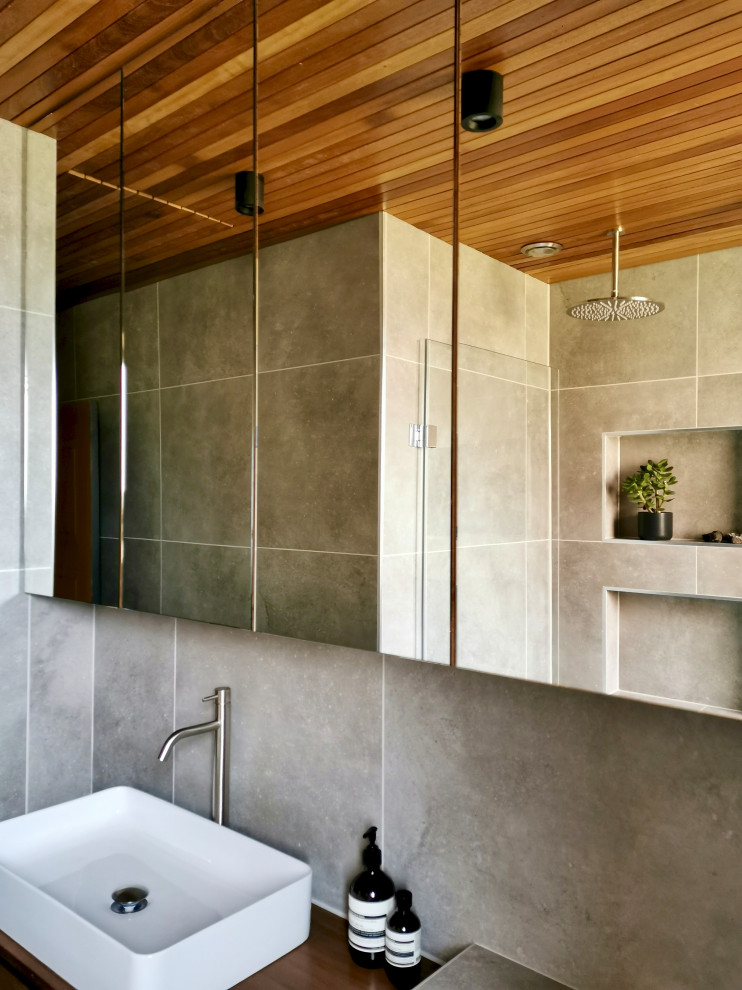 Photo of a small contemporary grey and brown bathroom in Other with flat-panel cabinets, brown cabinets, a built-in bath, a shower/bath combination, a wall mounted toilet, grey tiles, porcelain tiles, grey walls, porcelain flooring, grey floors, a single sink, a floating vanity unit and a timber clad ceiling.