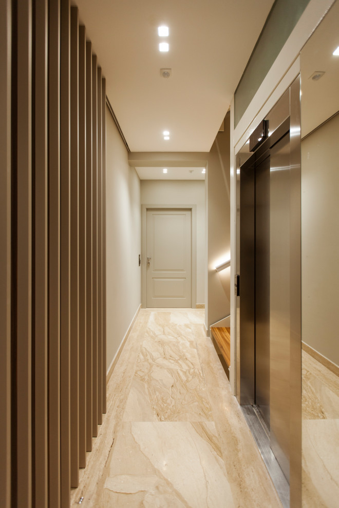 Cette photo montre un grand couloir moderne avec un mur beige, un sol en marbre, un sol beige et un plafond décaissé.