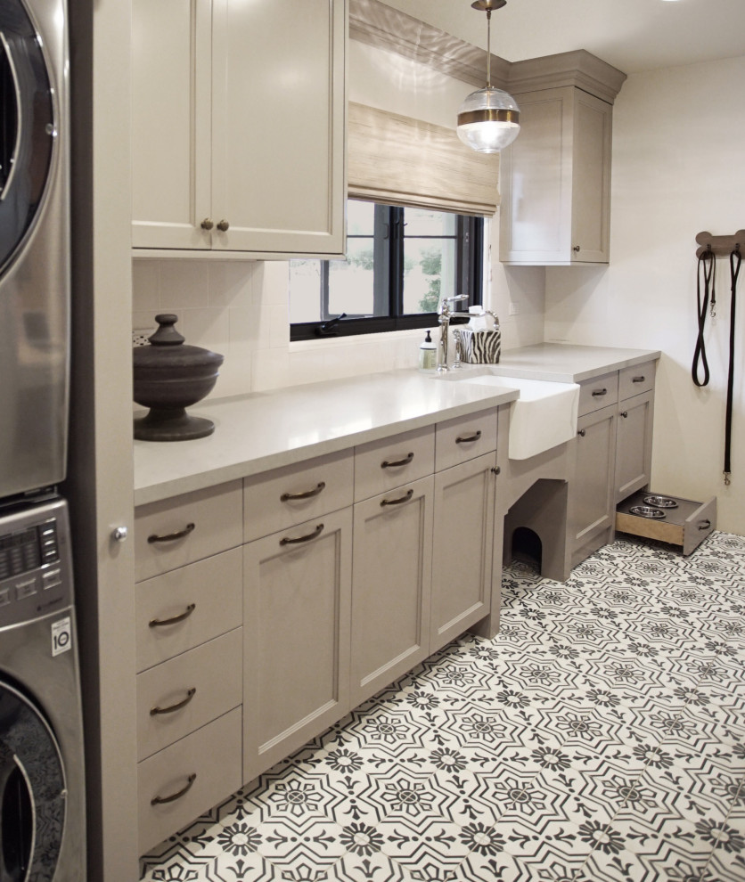 Inredning av en stor grå parallell grått tvättstuga enbart för tvätt, med en rustik diskho, luckor med infälld panel, grå skåp, bänkskiva i kvarts, vitt stänkskydd, stänkskydd i tunnelbanekakel, vita väggar, en tvättpelare och svart golv