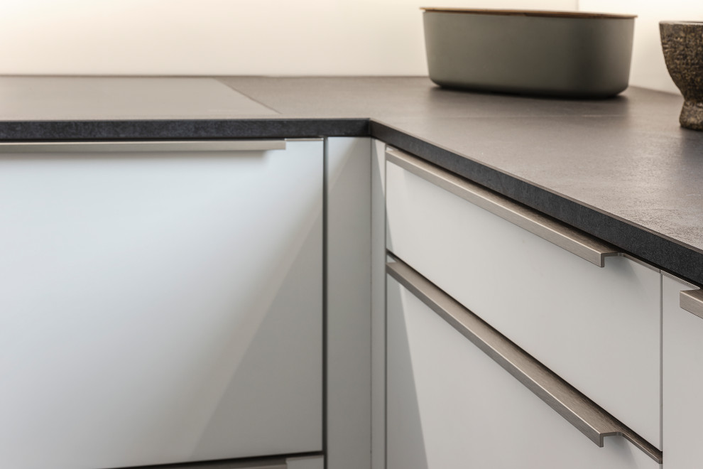 Photo of a mid-sized modern l-shaped open plan kitchen in Munich with an undermount sink, white cabinets, quartz benchtops, white splashback, glass sheet splashback, black appliances and grey benchtop.