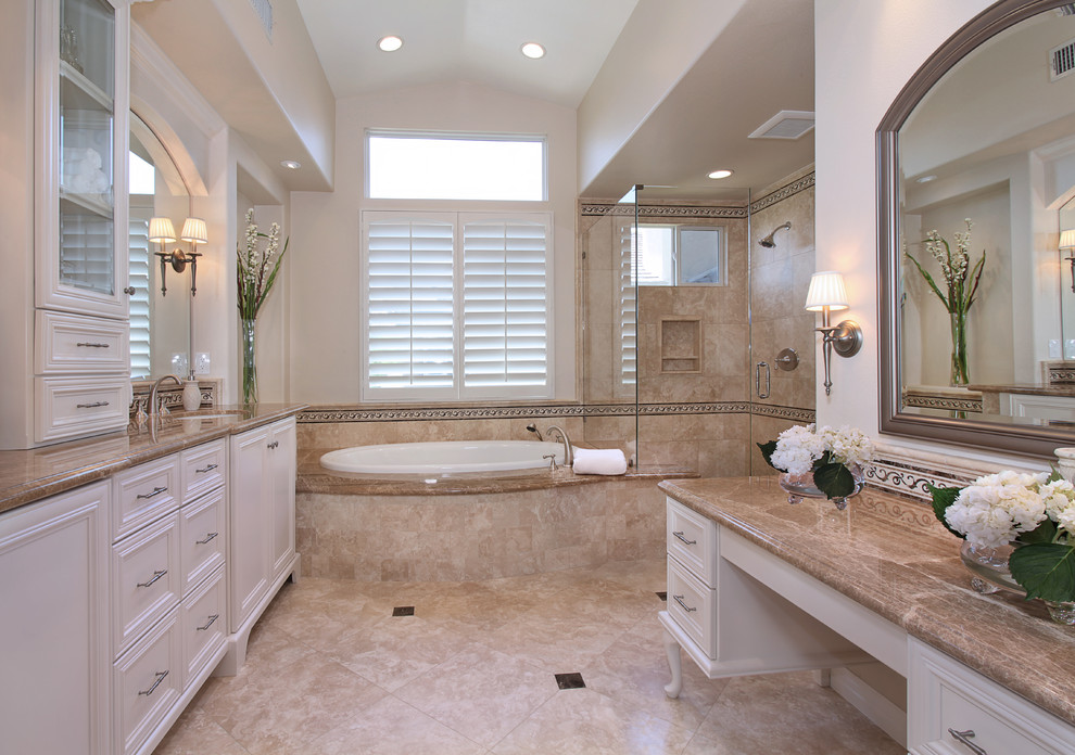 Design ideas for a large traditional master bathroom in Orange County with an undermount sink, raised-panel cabinets, white cabinets, marble benchtops, a drop-in tub, a corner shower, a one-piece toilet, beige tile, stone tile, beige walls and travertine floors.