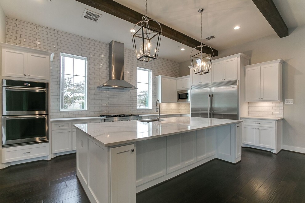Photo of a transitional u-shaped open plan kitchen in Houston with an undermount sink, shaker cabinets, white cabinets, white splashback, subway tile splashback, stainless steel appliances, with island and brown floor.