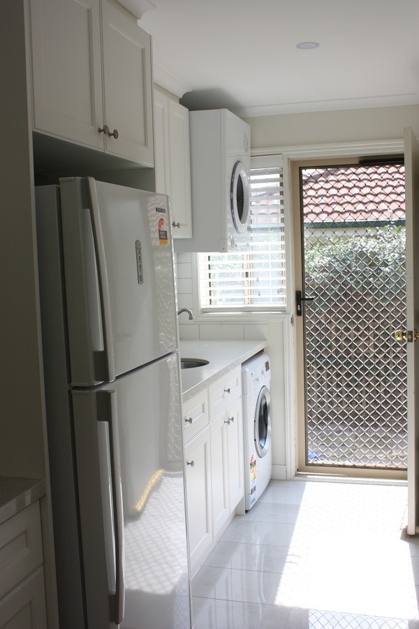 This is an example of a small modern single-wall utility room in Melbourne with an undermount sink, shaker cabinets, white cabinets, white walls, porcelain floors, a stacked washer and dryer and white floor.