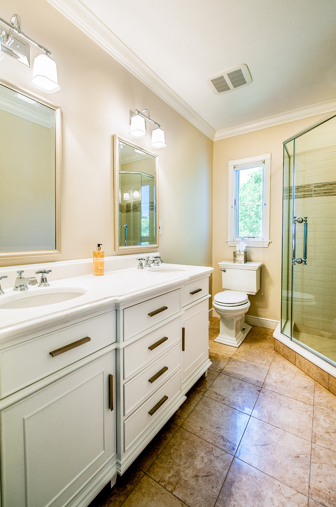 Inspiration for a mid-sized beach style 3/4 bathroom in Boston with beaded inset cabinets, white cabinets, a corner shower, a two-piece toilet, white tile, subway tile, beige walls, porcelain floors, an undermount sink, solid surface benchtops, beige floor and a hinged shower door.