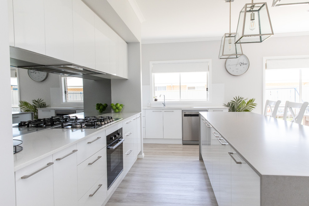 Mid-sized modern galley kitchen pantry in Other with white cabinets, solid surface benchtops, glass sheet splashback, stainless steel appliances, vinyl floors, with island, grey floor, grey benchtop and an undermount sink.