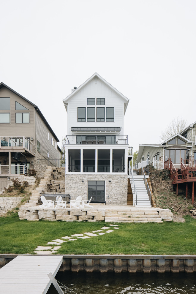 Backyard Exterior - Inspiration for a large coastal white four-story board and batten gable roof remodel in Grand Rapids with a mixed material roof and a black roof