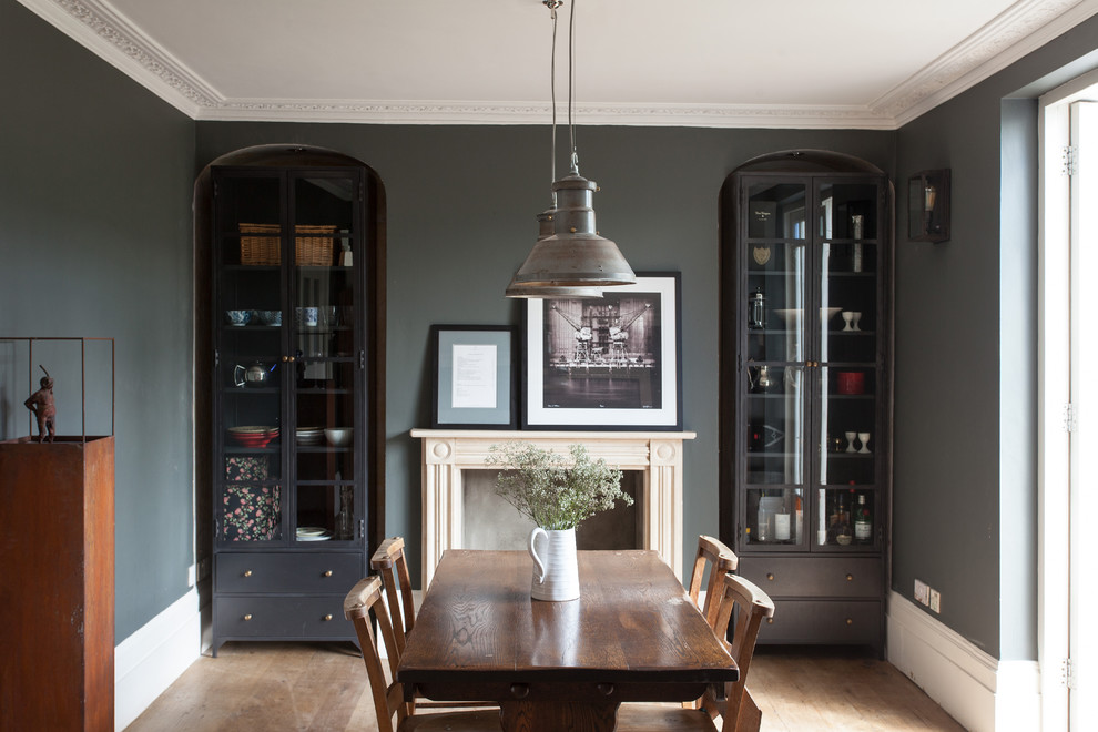 Photo of a transitional dining room in London with grey walls, medium hardwood floors, a standard fireplace and brown floor.