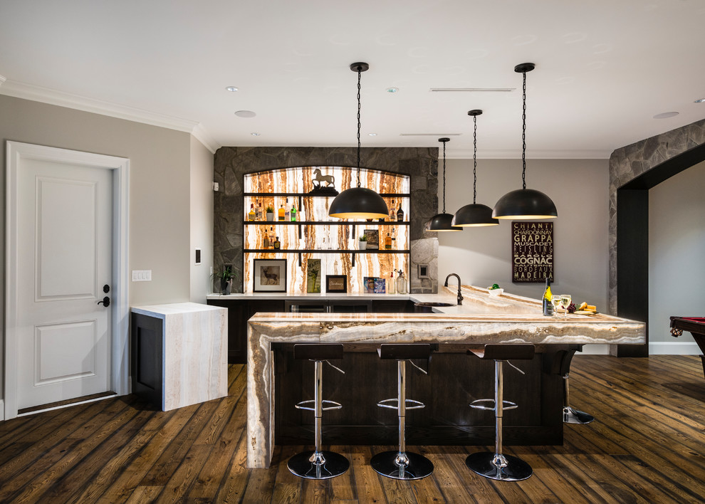 Photo of an expansive country u-shaped wet bar in Vancouver with a drop-in sink, shaker cabinets, dark wood cabinets, onyx benchtops, beige splashback, stone slab splashback, medium hardwood floors, brown floor and beige benchtop.