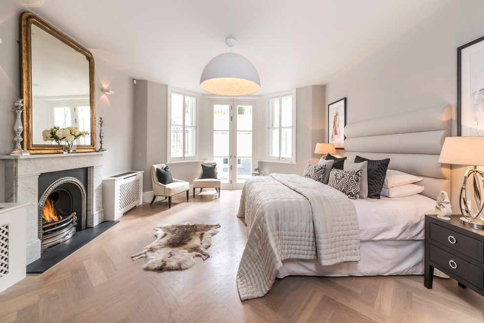 Large transitional master bedroom in London with beige walls, light hardwood floors, a standard fireplace and beige floor.