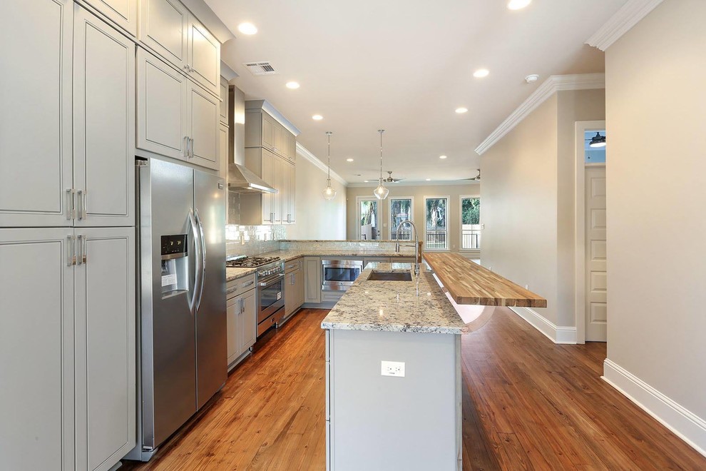 This is an example of a large transitional single-wall separate kitchen in New Orleans with an undermount sink, louvered cabinets, beige cabinets, granite benchtops, beige splashback, brick splashback, stainless steel appliances, medium hardwood floors, with island and brown floor.